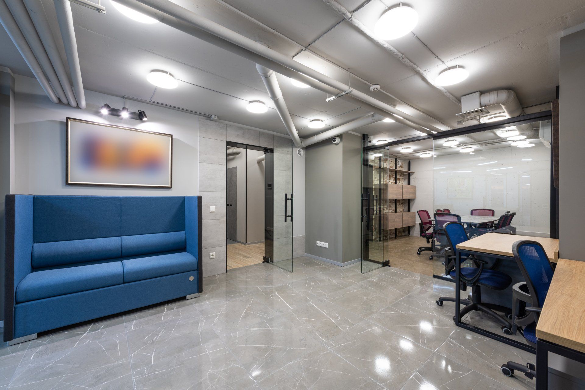 Office interior with blue sofa, glass doors, and desks.