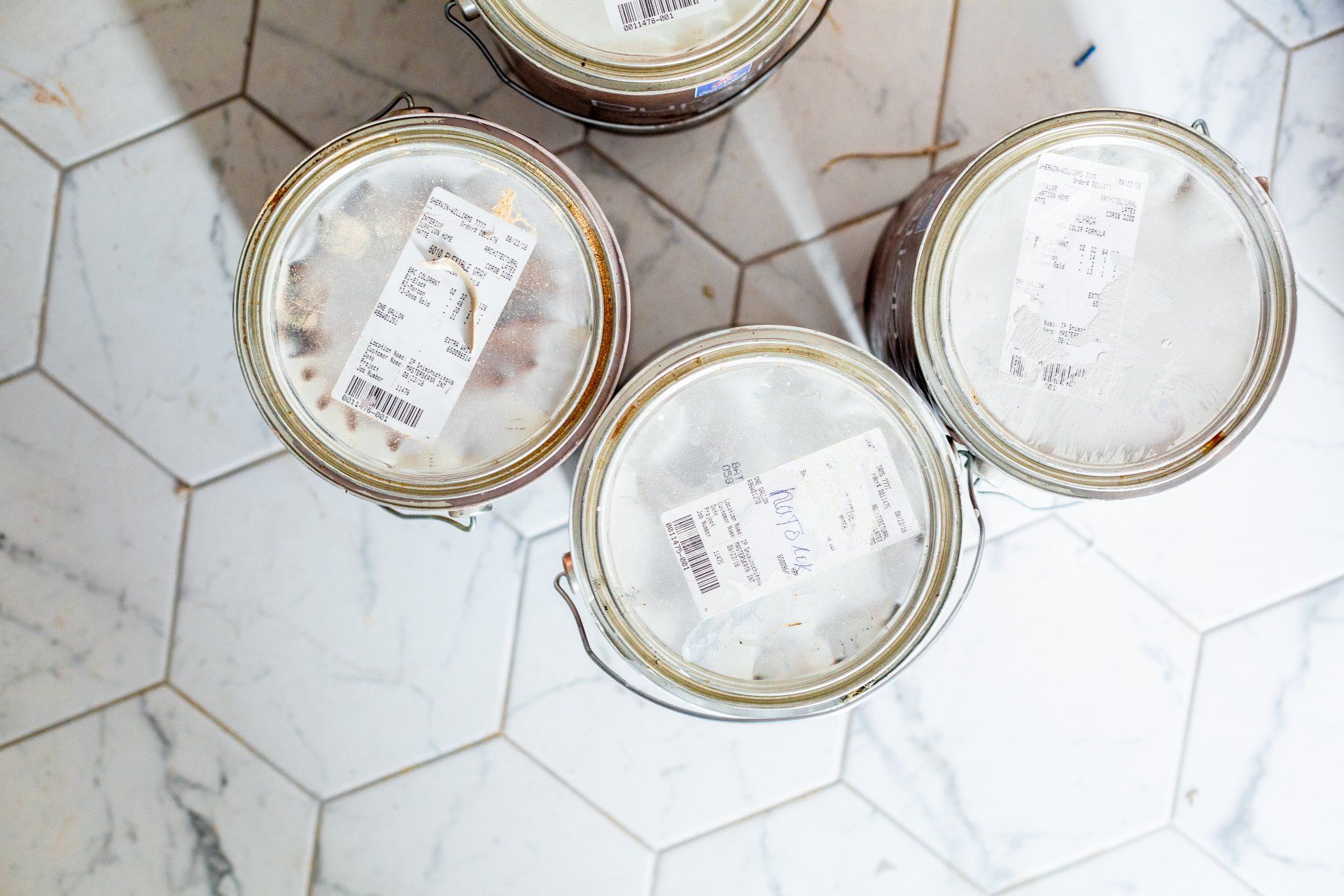 Overhead view of four paint cans on a white and gray tiled floor; each can has a label visible on the top.